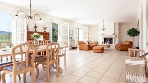 Een ruime woonkamer met een eettafel, houten stoelen, een bank en een open haard.