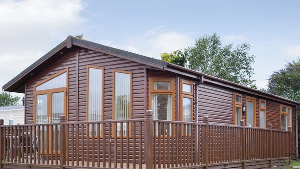 Une cabane en bois dotée d’une terrasse entourée d’une clôture, de grandes fenêtres et d’un toit en pente.