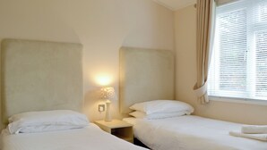 Une chambre d’hôtel avec deux lits, une table de chevet avec une lampe et une fenêtre avec des stores.