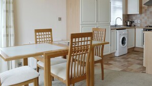 Une cuisine compacte équipée d’un lave-linge, d’une table à manger avec des chaises et d’un luminaire fixé au mur.