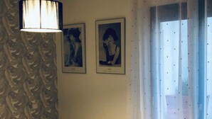 Une chambre d’hôtel avec un lit, une table de chevet, une lampe, deux tableaux encadrés et une fenêtre avec des rideaux.