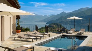 A poolside area with lounge chairs and umbrellas, overlooking a mountainous landscape and a body of water. - Villa Sonni - Four Bedroom Villa, Sleeps 8 (Bellagio)