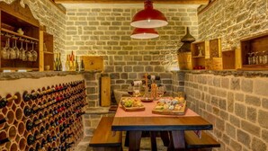 A rustic stone-walled room with a wooden table set for a meal, wine bottles on shelves, and a hanging red light fixture. - Villa Sonni - Four Bedroom Villa, Sleeps 8 (Bellagio)