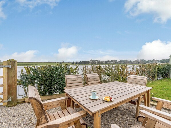 Une table en bois installée à l’extérieur, avec des bancs, une assiette de nourriture et une tasse.