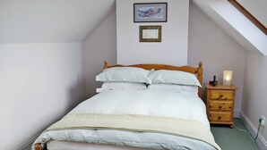 Una cama individual con estructura de madera, una mesita de noche con lámpara, y un cuadro enmarcado en la pared.
