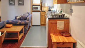 Un espacio habitable compacto con sofá, una pequeña mesa de comedor, una kitchenette con estufa y microondas, y un banco de madera.