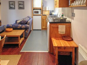 A compact living space with a sofa, a small dining table, a kitchenette with a stove and microwave, and a wooden bench. - Haven Cottage - E4342 (Holy Island)