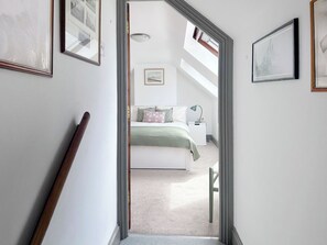 A hallway leading to a bedroom with a bed, a nightstand, and a lamp. - Haven Cottage - E4342 (Holy Island)