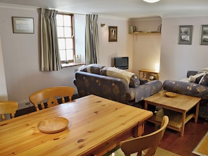 A living room with a sofa, a wooden table, a television, and a window with curtains. - Haven Cottage - E4342 (Holy Island)