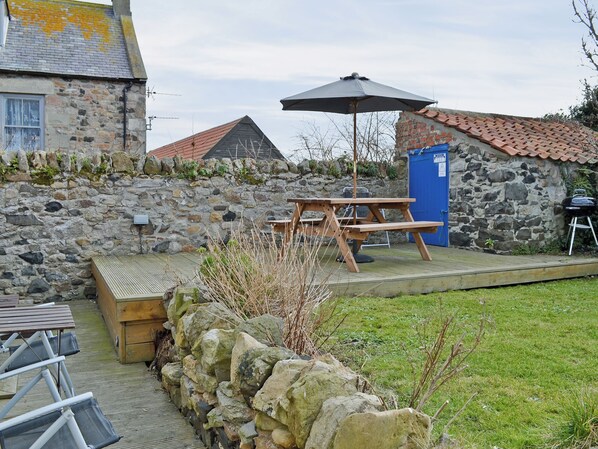 A stone wall, a wooden bench, a picnic table, a barbecue grill, and a blue door. - Haven Cottage - E4342 (Holy Island)
