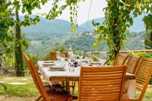 An outdoor dining table set with chairs, surrounded by greenery and a mountainous backdrop.
