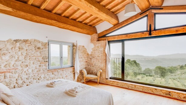A bedroom with a stone wall, wooden beams, a large window with a view, a bed, and a chair. - Villa Todari - Three Bedroom Villa, Sleeps 10 (Torricella in Sabina)
