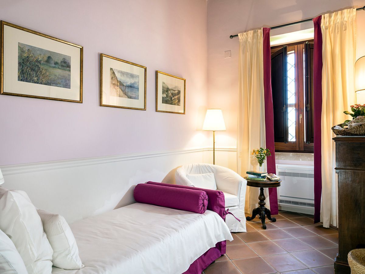 A hotel room with a bed, a chair, a table with a lamp, and a window with curtains.