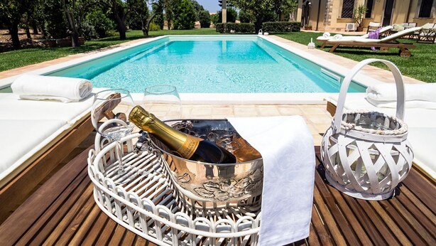 A poolside area with a wooden deck, a metal wine cooler with a bottle, and a lantern.