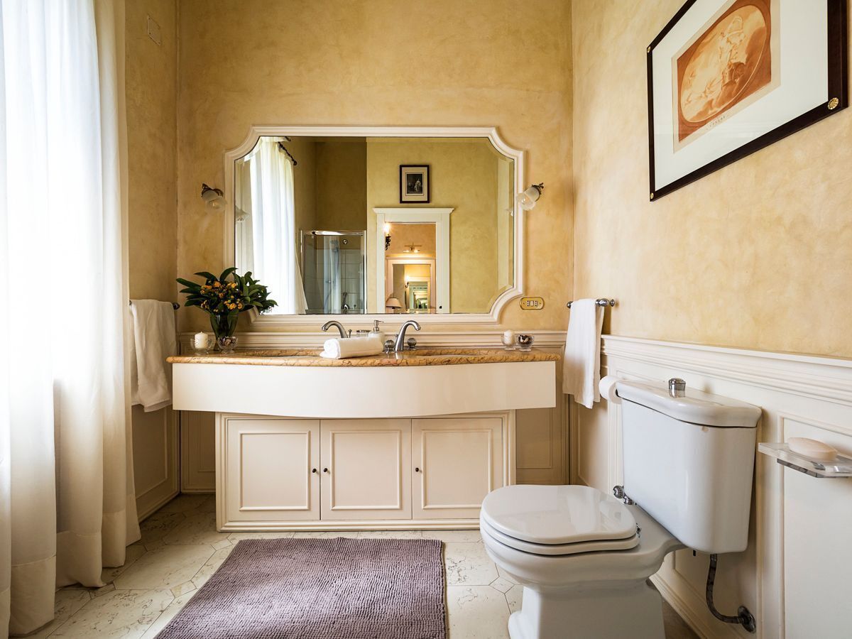 Een badkamer met een grote spiegel, een wastafel, een toilet en een lijst met een foto aan de muur.