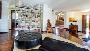 A spacious living room with a black leather ottoman, a wooden statue, and a bookshelf filled with books.
