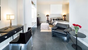 A modern hotel room with a desk, chair, bed, and a small round table with a vase of flowers.