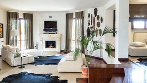 A modern living room with a fireplace, a large potted plant, and a flat-screen TV.
