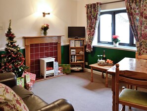A living room with a fireplace, a Christmas tree, a television, and a window with curtains. - 1 bedroom accommodation in Wheddon Cross, Exmoor (Wheddon Cross, Exmoor)