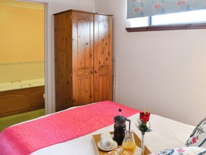 Una camera da letto con un letto, un armadio in legno, una finestra con tenda floreale e un vassoio colazione con caffettiera, bicchiere di succo d'arancia e una rosa.