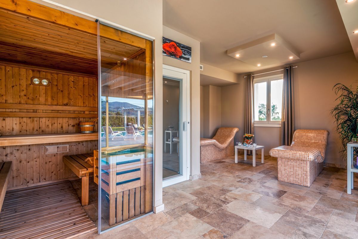 A sauna room with wooden walls and a glass door, a bench, and a small table with a vase.
