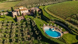 An aerial view of a villa with a swimming pool surrounded by manicured gardens and olive groves.