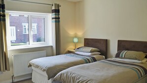 A bedroom with two beds, a window with curtains, a radiator, and a bedside lamp.
