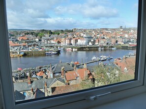 Une vue sur un port, avec des bateaux, des bâtiments et le clocher d’une église au loin.