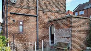 A brick building with a small arched entrance, a bench, and a metal fence.