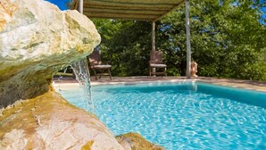A clear blue pool with a rock formation in the foreground, a covered seating area, and trees in the background. - Villa Tirelli - Five Bedroom Villa, Sleeps 10 (San Casciano dei Bagni)