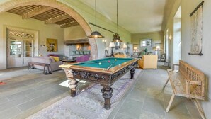 Une pièce spacieuse équipée d’une table de billard, de sièges confortables et d’une grande porte en arc de cercle.
