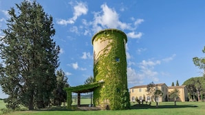 Une tour cylindrique recouverte de lierre, un belvédère et un bâtiment à toit de tuiles, le tout situé dans un champ verdoyant.