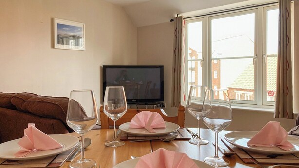 A dining area with a table set for four, a television, and a window with curtains.
