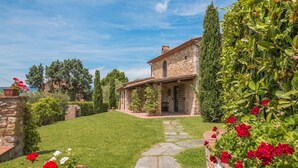 Una casa de piedra con un camino empedrado que lleva a la entrada, rodeada de vegetación y plantas en flor.