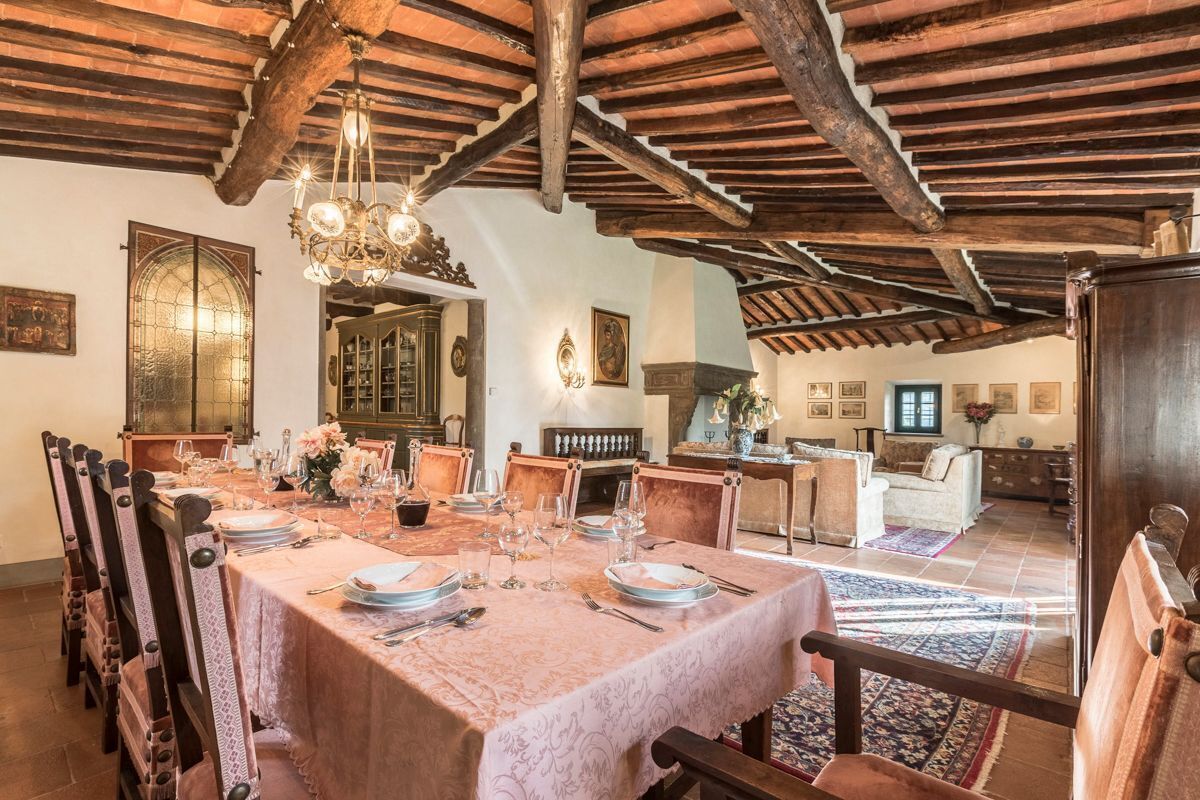 A dining room with a long table set for a meal, wooden beams on the ceiling, and a chandelier.