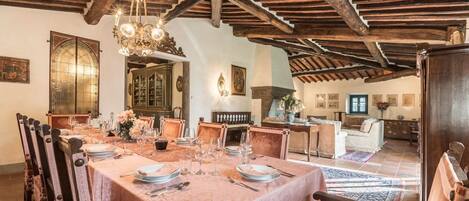 A dining room with a long table set for a meal, wooden beams on the ceiling, and a chandelier.