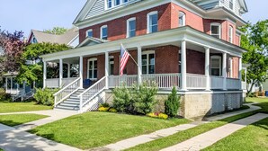 A two-story brick house with a white porch, a flag, and a staircase leading to the entrance. - Serene Beach Haven in Cape Charles (Cape Charles)