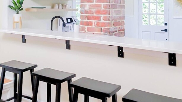 A kitchen with a brick chimney, white shelves, and black bar stools. - Serene Beach Haven in Cape Charles (Cape Charles)