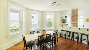 A dining area with a long table, six chairs, and a brick chimney. - Serene Beach Haven in Cape Charles (Cape Charles)