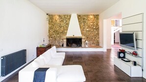 Un salon moderne avec une cheminée en pierre, un canapé blanc et un téléviseur posé sur une console blanche.