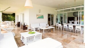 Un vaste espace de vie comprenant un canapé blanc, une table à manger et des chaises. Une grande fenêtre offre une belle vue sur l’extérieur et permet à la lumière naturelle d’entrer.