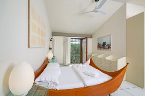 Una camera da letto con un'amaca, una ventola a soffitto, una finestra con tende, un comodino e un quadro appeso al muro.