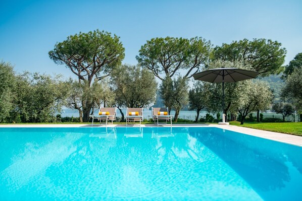 A swimming pool with lounge chairs and umbrellas, surrounded by trees and a view of the water.