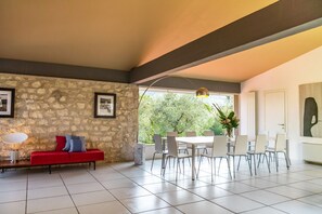Un interno moderno con una parete in pietra, un divano rosso, un tavolo da pranzo con sedie e un'ampia finestra vista alberi.