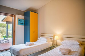 A hotel room with two beds, a wardrobe, a table, and a view of the outdoors.