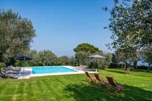 Ein Schwimmbecken mit Liegestühlen und Sonnenschirmen, umgeben von Bäumen und Gras.