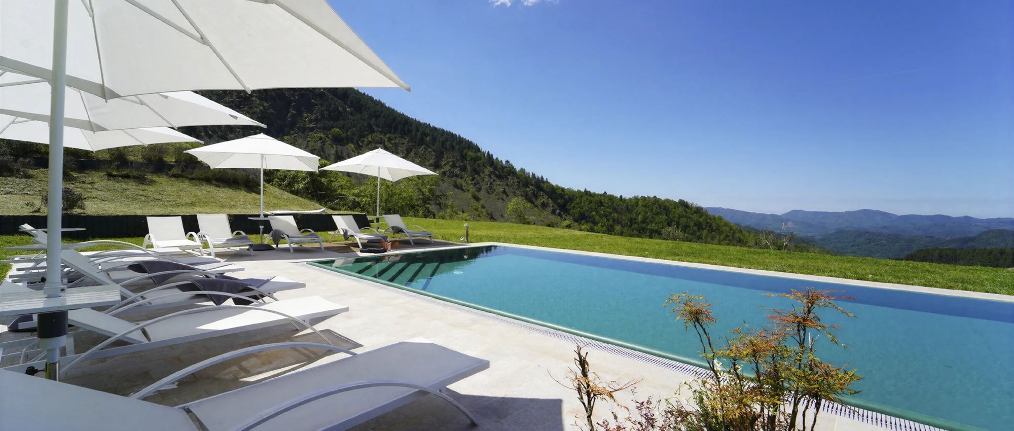 A swimming pool with lounge chairs and umbrellas, surrounded by a mountainous landscape.