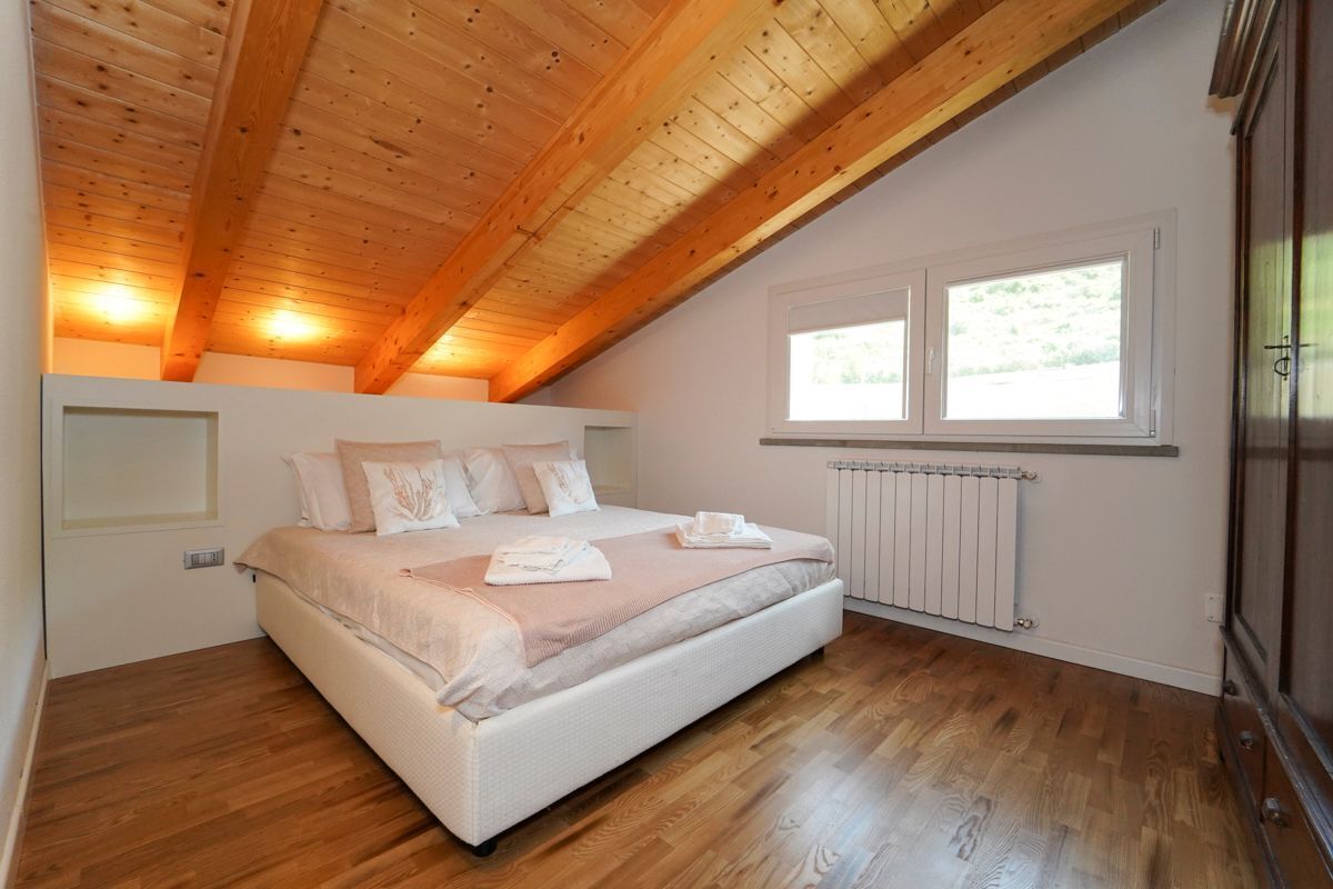A bedroom with a wooden ceiling, a large bed, a window, and a radiator.