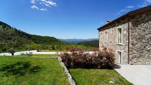 A stone building with a stone facade, a small garden with red flowers, and a view of green hills in the background. - Villa Sasseta - Eight Bedroom Villa, Sleeps 16 (Zignago)