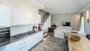 A modern kitchen with white cabinets, a gas stove, and a wooden countertop. There is a staircase leading to a living area with a sofa and a TV. - Villa Sasseta - Eight Bedroom Villa, Sleeps 16 (Zignago)